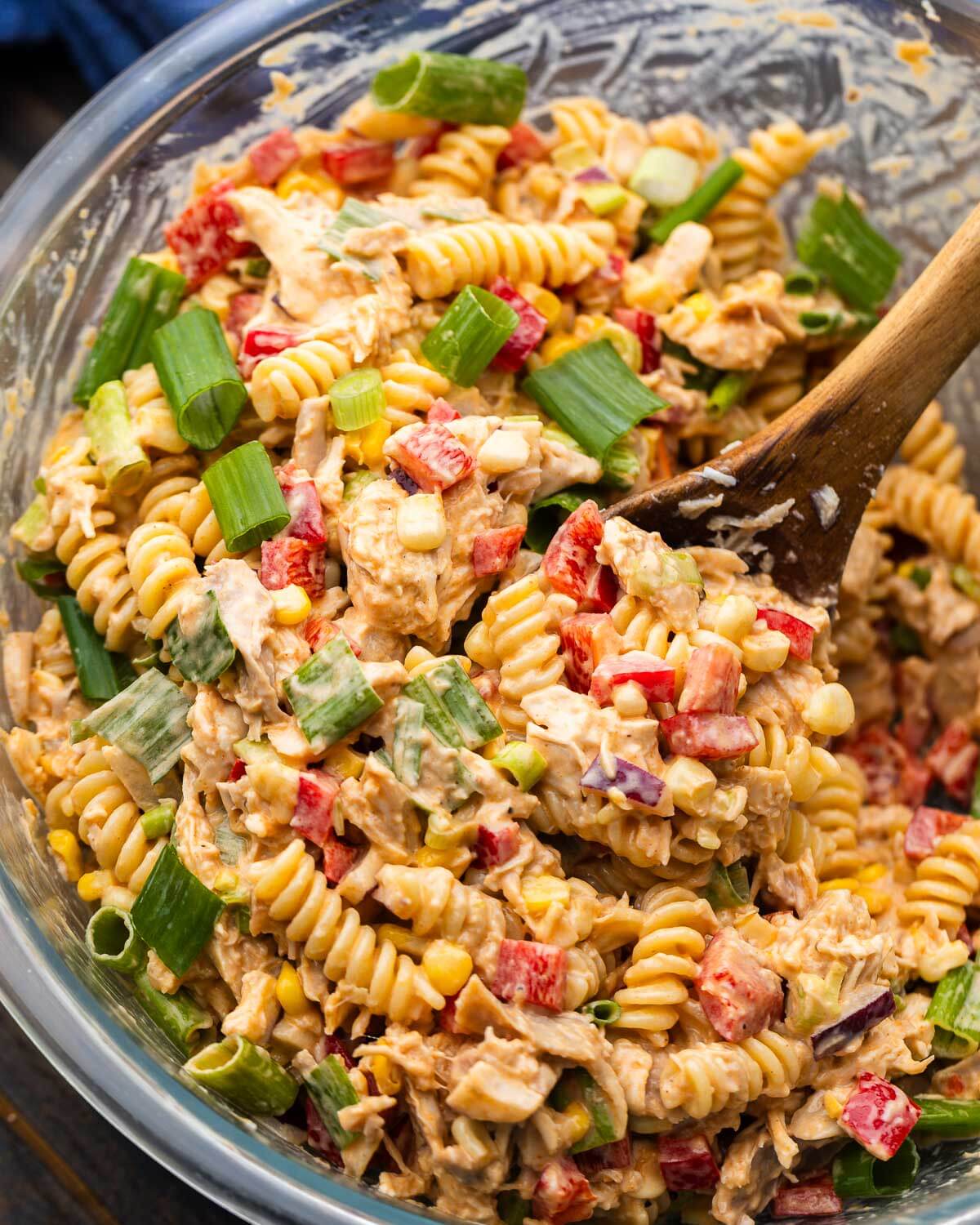 Spoon scooping barbecue chicken pasta salad out of bowl.