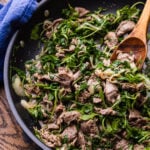 Sauteed beef with arugula in large black pan.