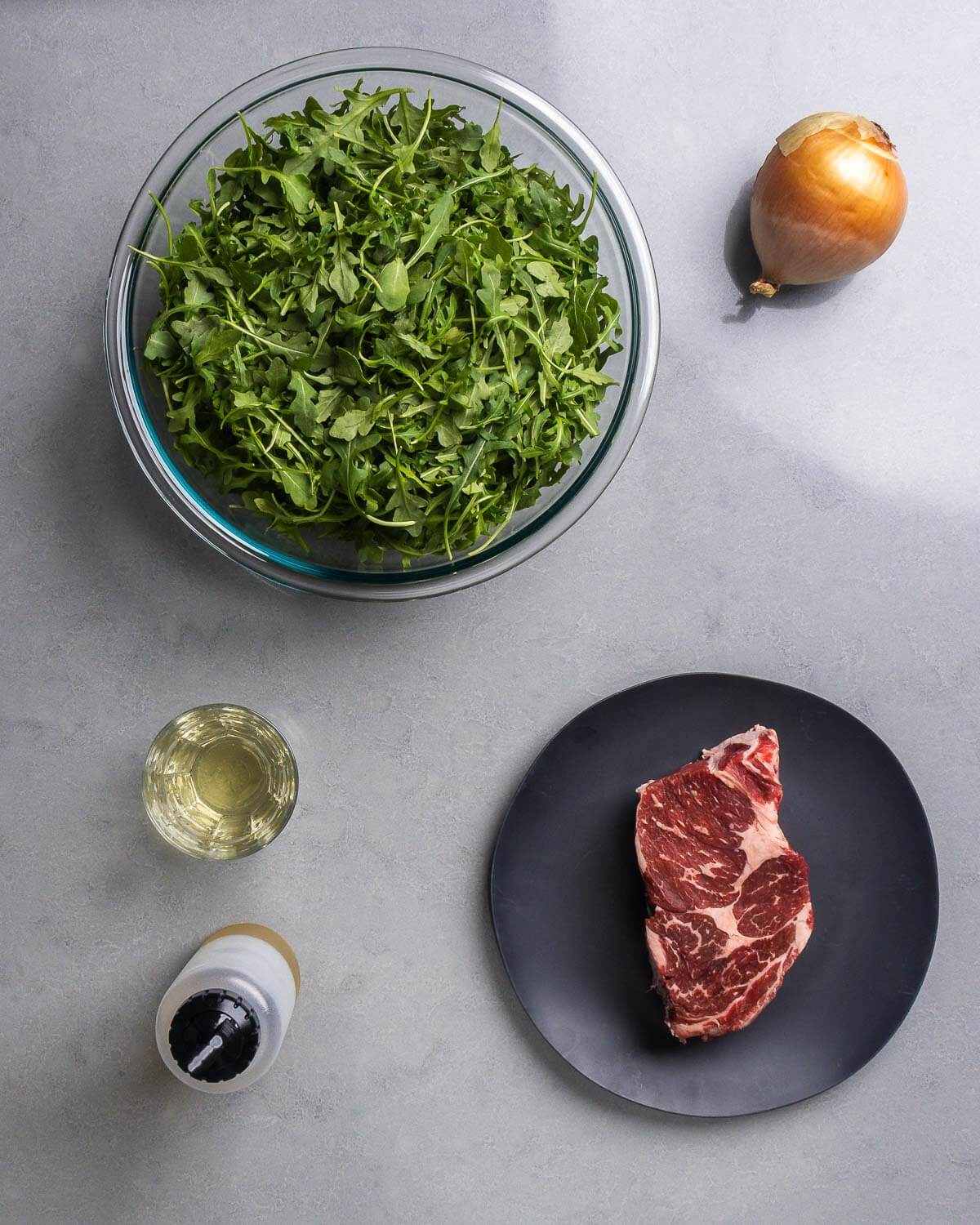 Ingredients shown: baby arugula, onion, white wine, olive oil, and ribeye steak.