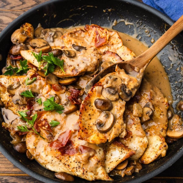 Large black pan with spoon scooping piece of chicken marsala.