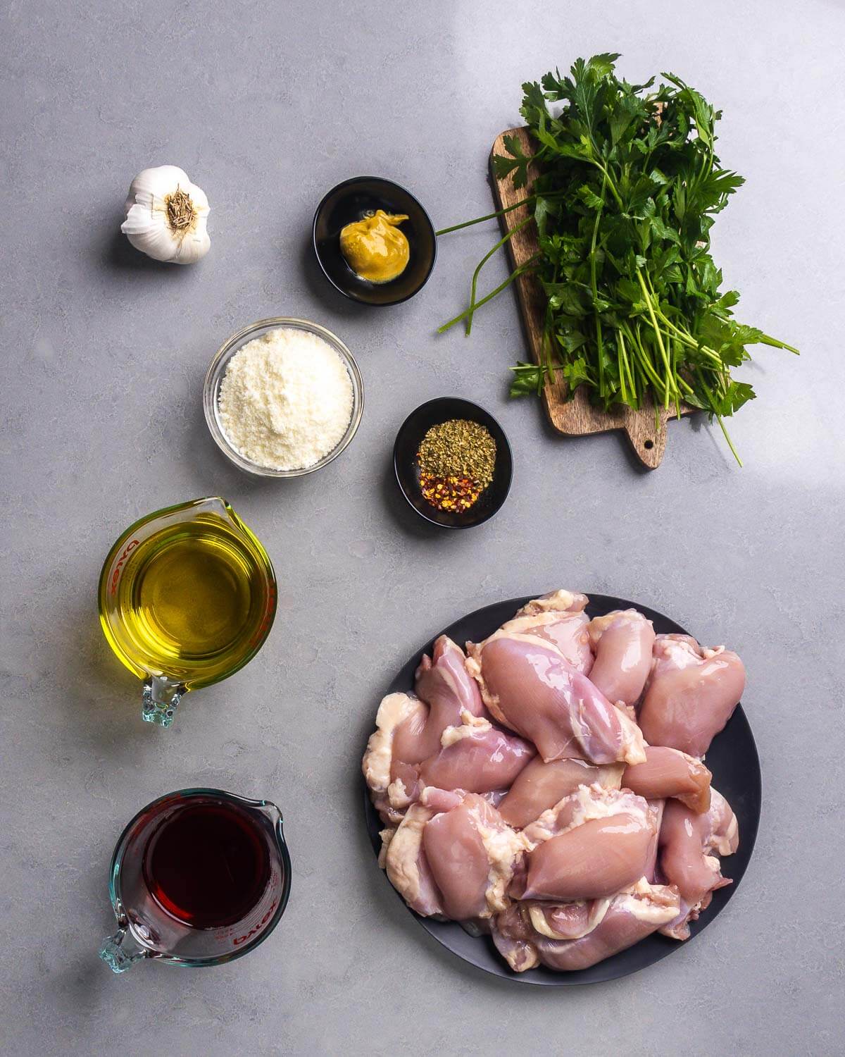 Ingredients shown: garlic, Dijon mustard, parsley, pecorino romano cheese, oregano, hot red pepper flakes, olive oil, red wine vinegar, and boneless skinless chicken thighs.