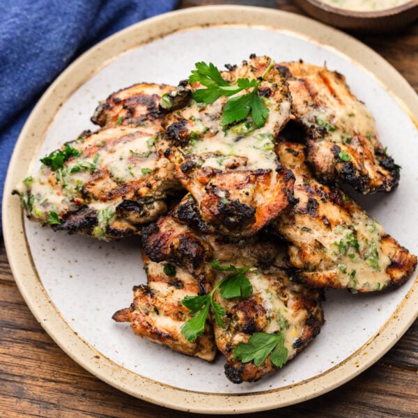 Plate of grilled chicken thighs with Italian dressing and parsley garnish.