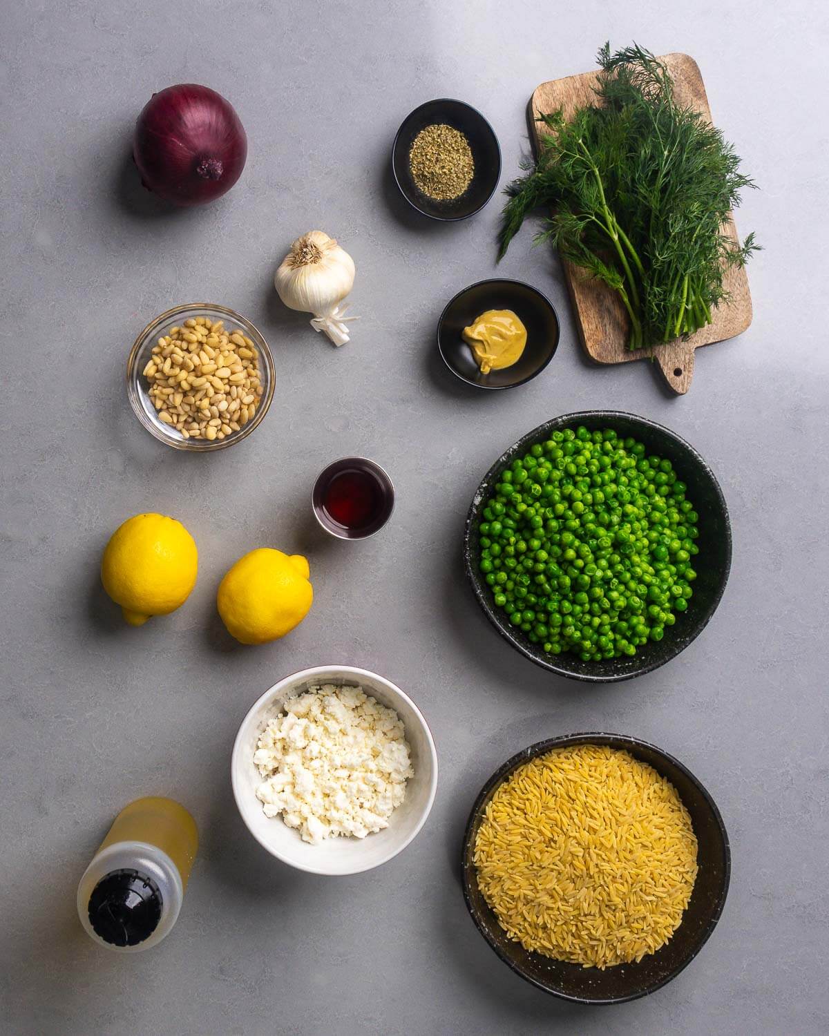 Ingredients shown: small onion, garlic, oregano, dill, Dijon mustard, pine nuts, red wine vinegar, lemons, peas, olive oil, feta cheese, and orzo pasta.