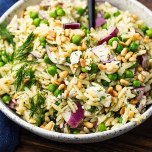 White bowl with lemon herb orzo salad topped with toasted pine nuts.