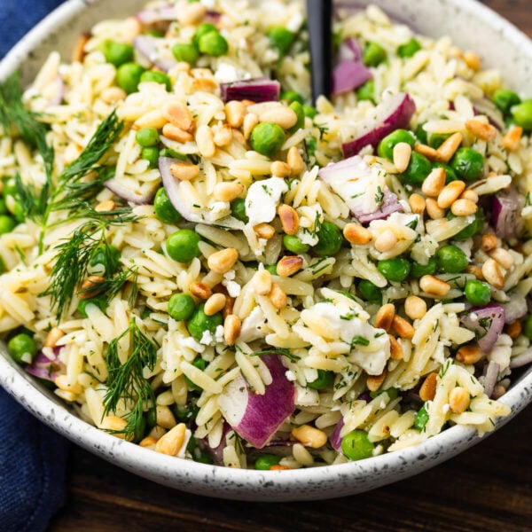 White bowl with lemon herb orzo salad topped with toasted pine nuts.