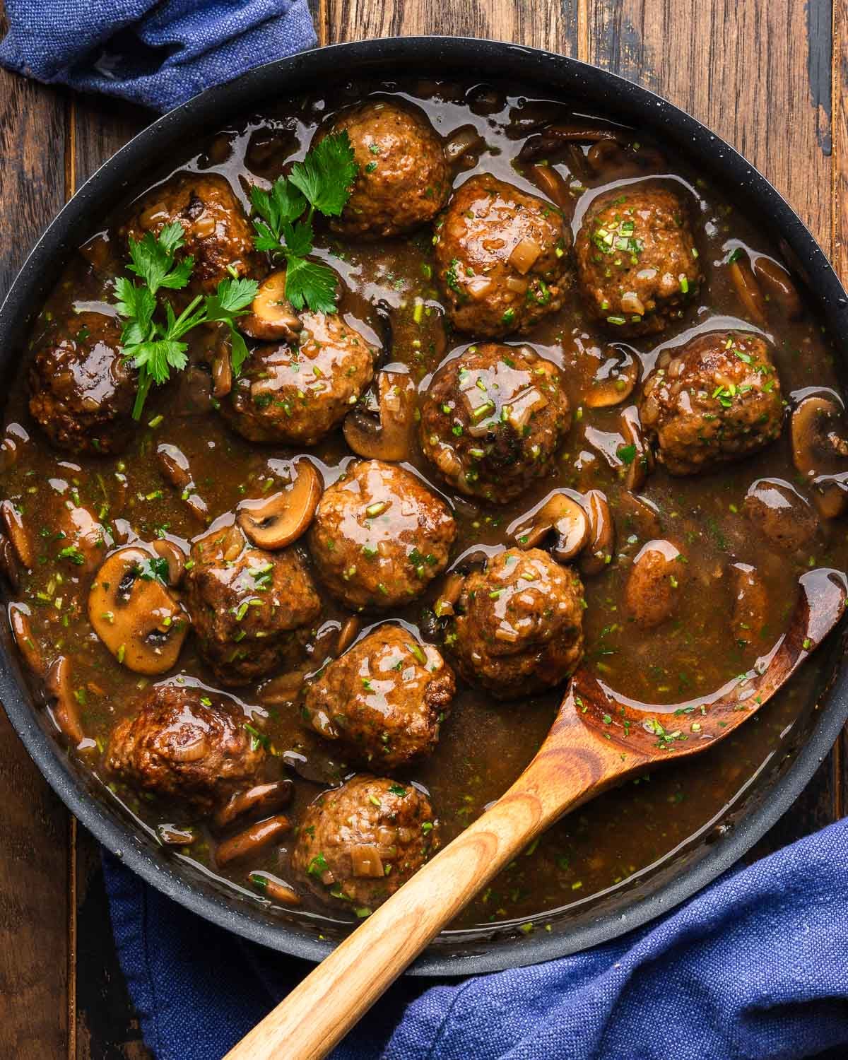 Large black pan with marsala meatballs topped with parsley.