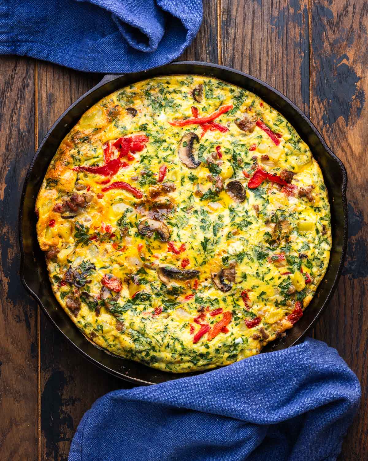 Large cast iron pan with sausage mushroom frittata on wood table.