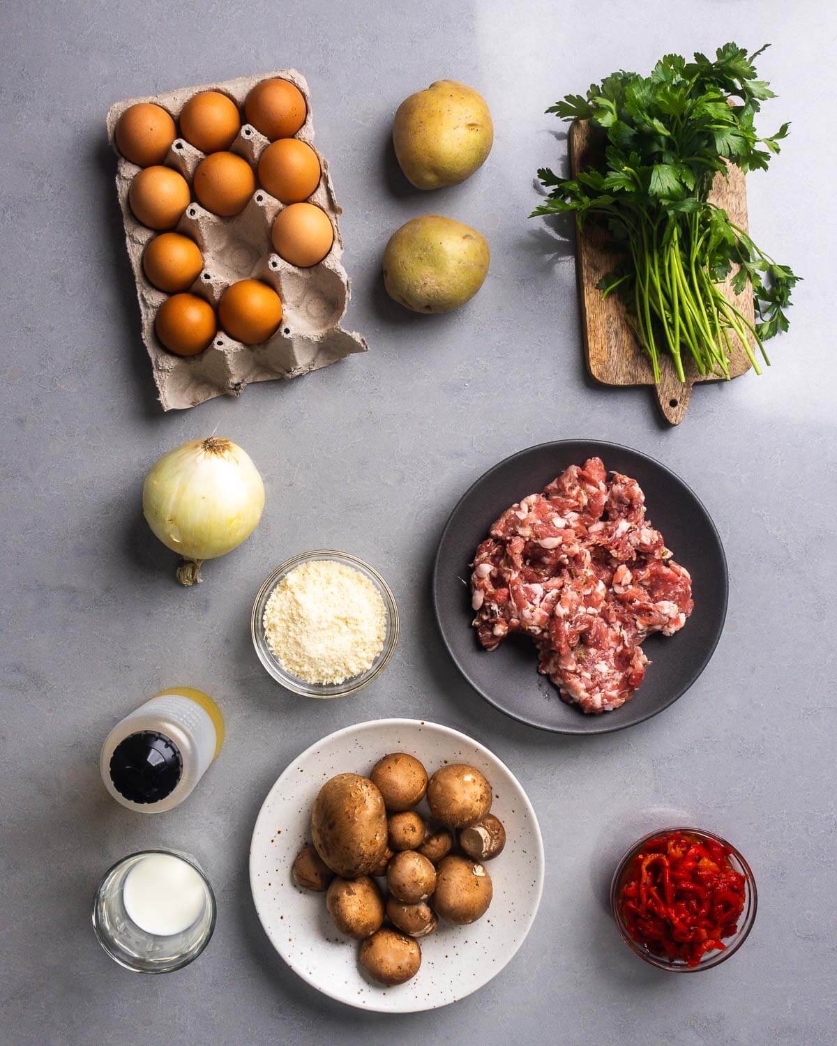 Ingredients shown: eggs, potatoes, parsley, onion, parmesan, bulk Italian sausage, olive oil, milk, mushrooms, and roasted red peppers.