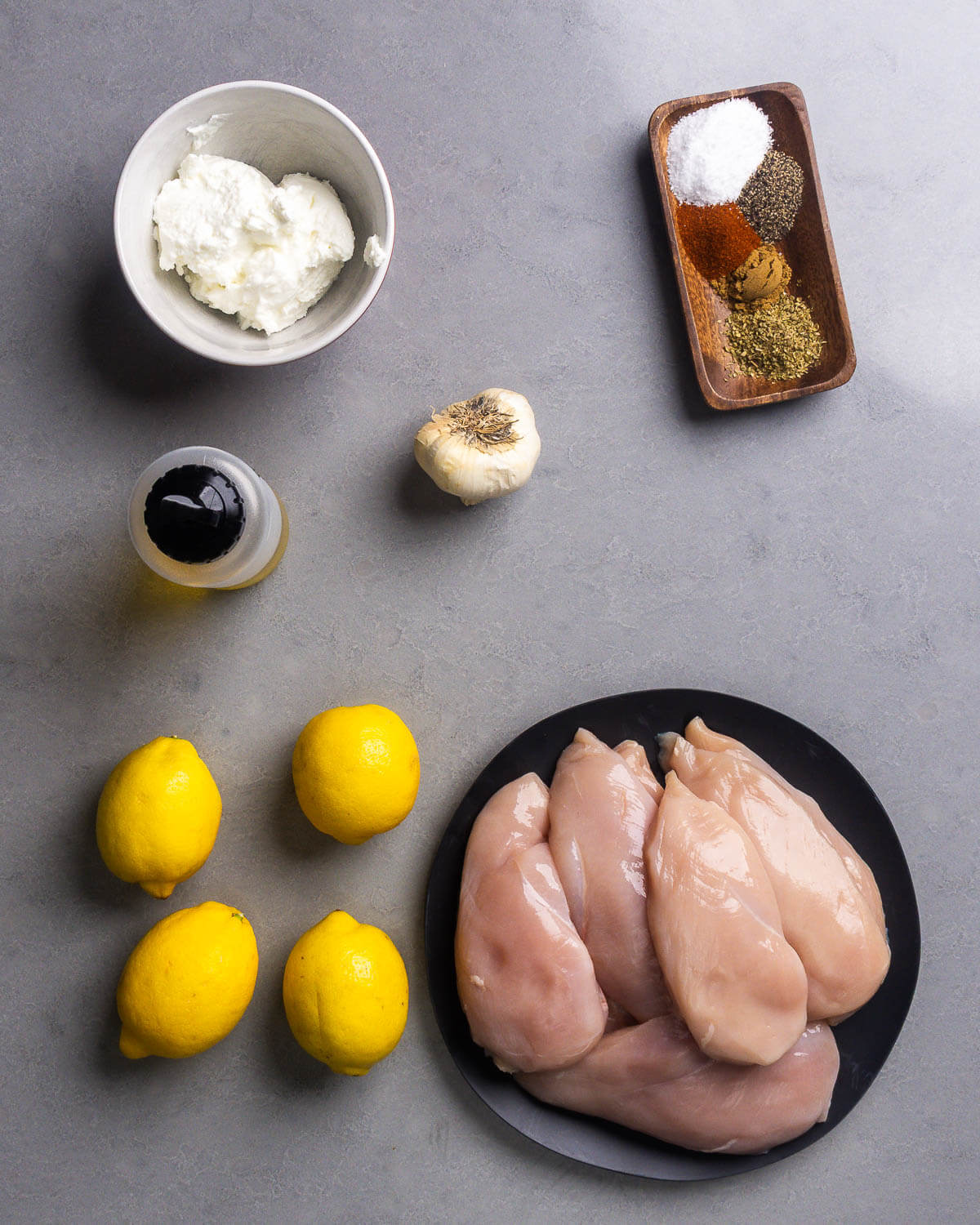 Ingredients shown: Greek yogurt, olive oil, garlic, salt, pepper, paprika, cumin, oregano, lemons, and chicken breasts.