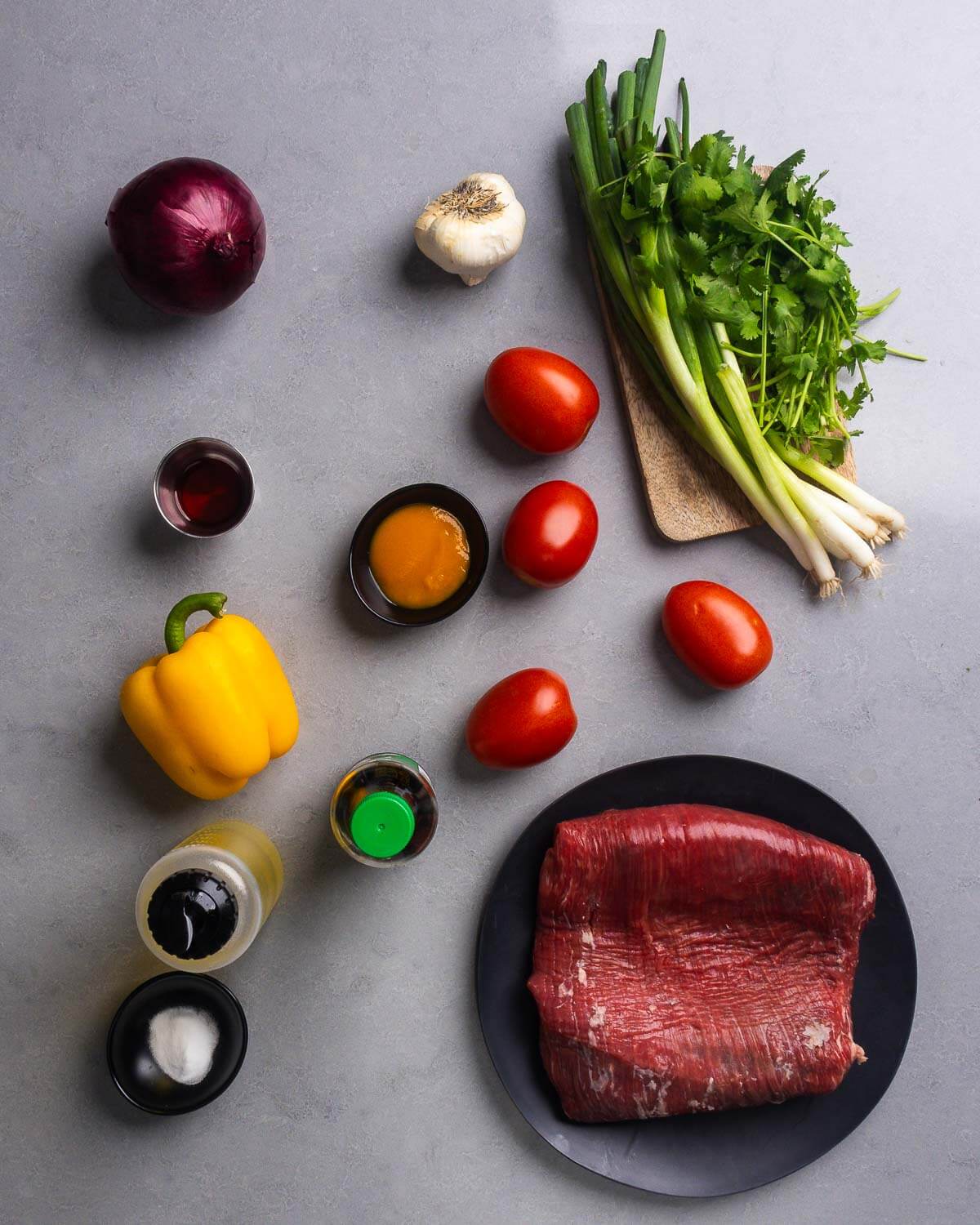 Ingredients shown: red onion, garlic, green onion, cilantro, red wine vinegar, aji amarillo paste, plum tomatoes, bell pepper, soy sauce, neutral oil, baking soda, and flank steak.