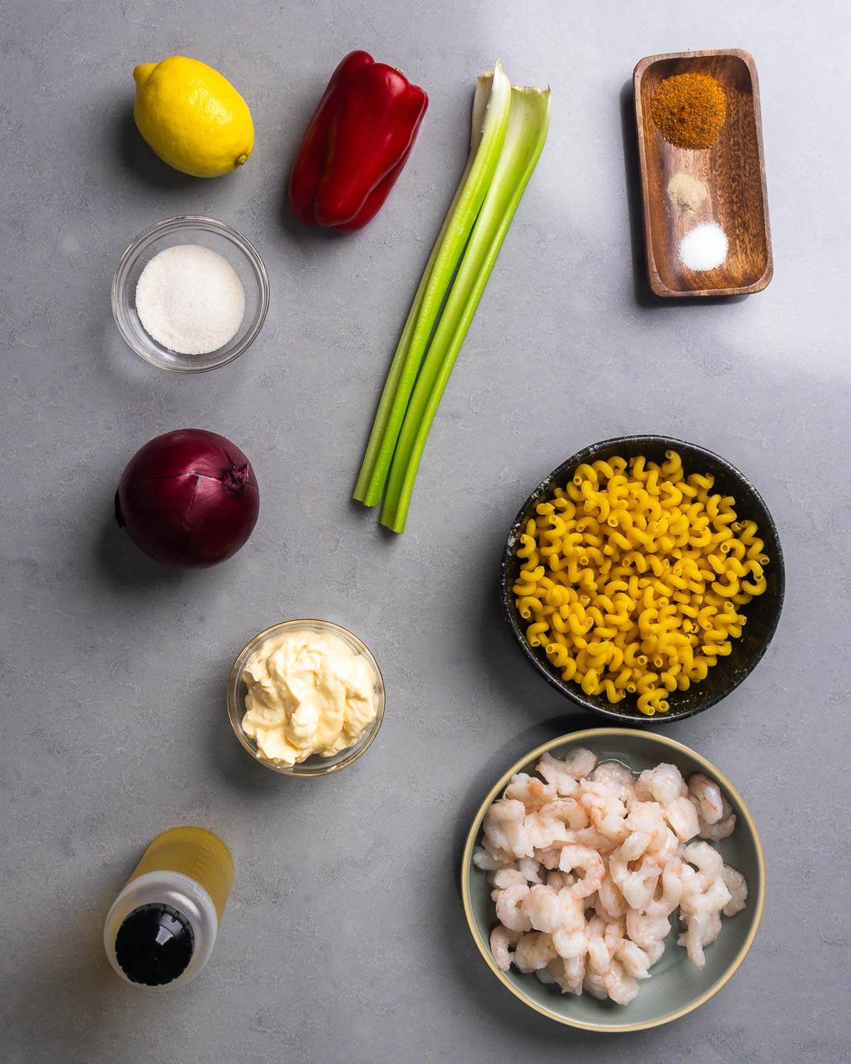 Ingredients shown: lemon, bell pepper, sugar, celery, Old Bay seasoning, white pepper, salt, red onion, mayonnaise, macaroni, olive oil, and shrimp.