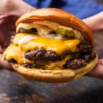 Hands holding a smash burger.