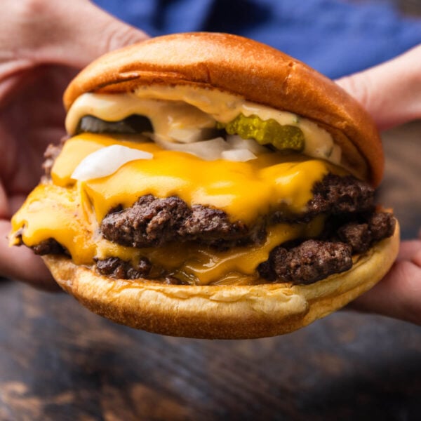 Hands holding a smash burger.