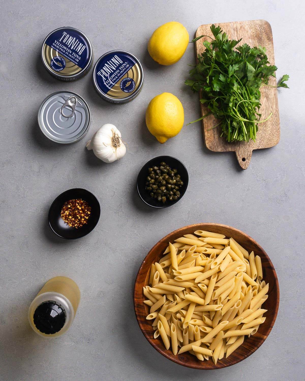 Ingredients shown: canned yellowfin tuna, lemons, garlic, capers, parsley, hot red pepper flakes, olive oil, and penne pasta.