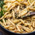 Spoon scooping tuna pasta in white sauce out of pan.
