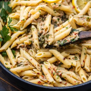 Spoon scooping tuna pasta in white sauce out of pan.