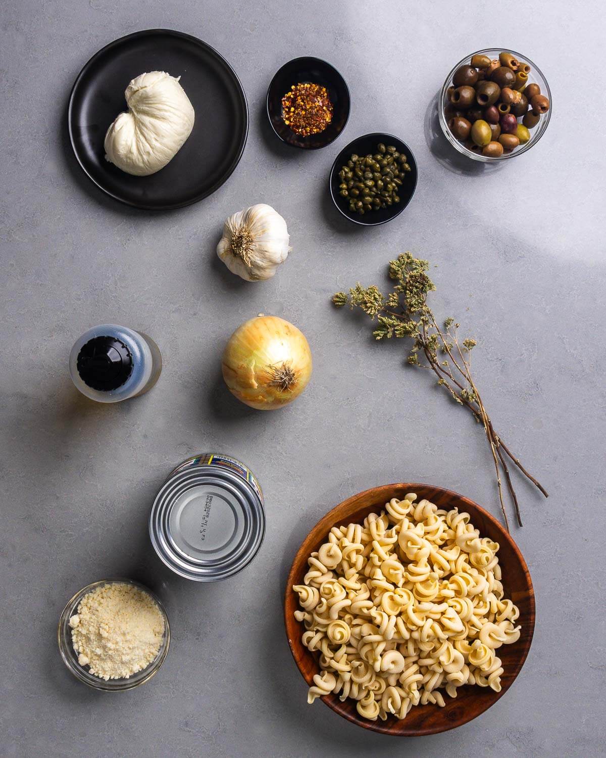 Ingredients shown: fresh mozzarella, hot red pepper flakes, capers, olives, garlic, olive oil, onion, Sicilian oregano, Parmigiano Reggiano, canned tomatoes, and pasta.