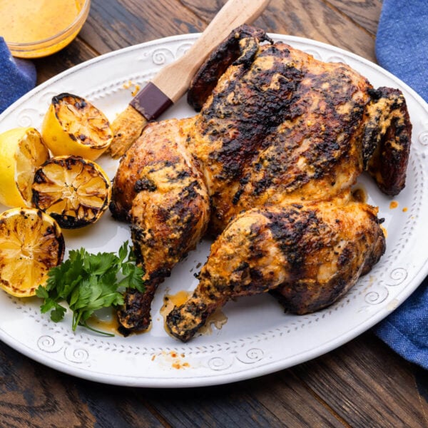 Large platter with peri peri chicken and grilled lemons.