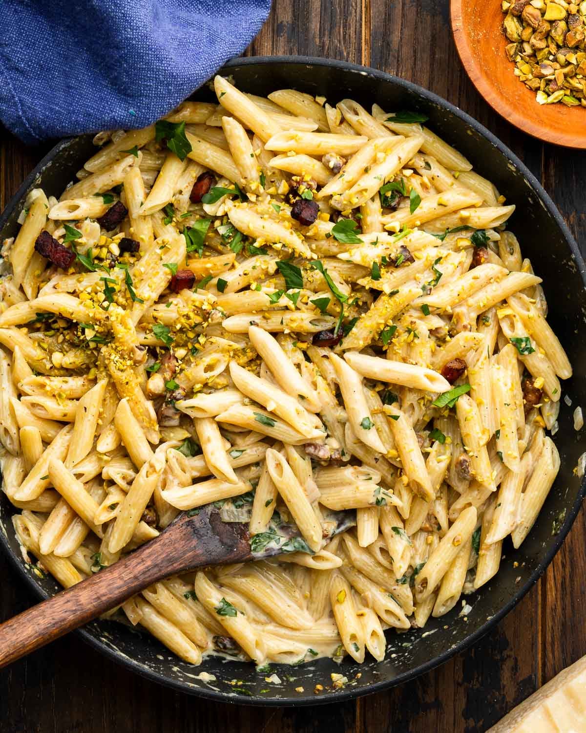 Pan with pistachio pasta and bowl of chopped pistachios on the side.