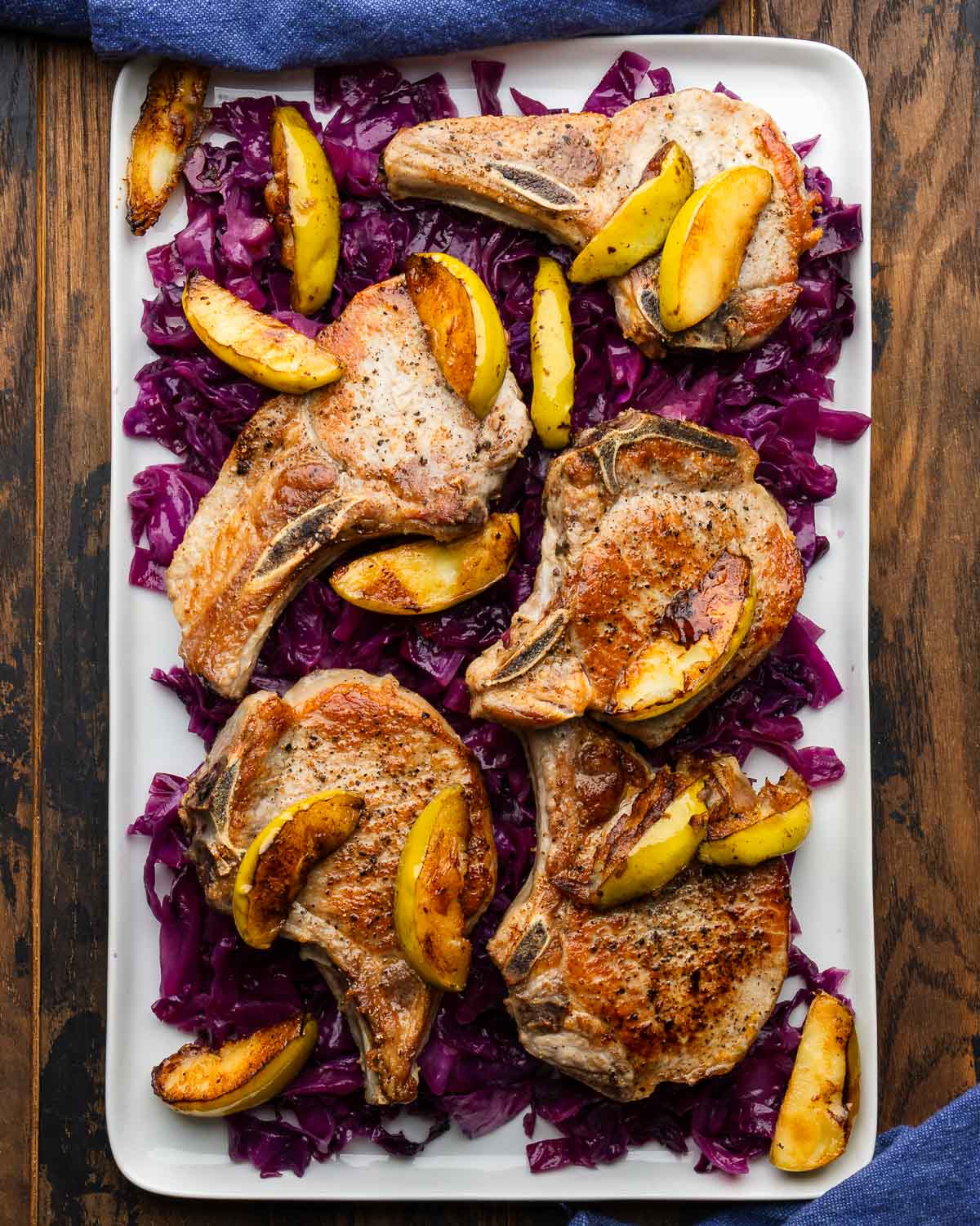 Large white platter braised cabbage topped with seared pork chops and apples.