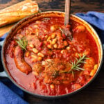 Dutch oven with braised ribs, Italian sausage, and beans garnished with rosemary sprigs.