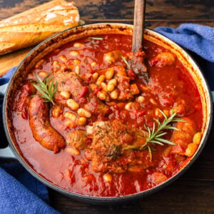 Dutch oven with braised ribs, Italian sausage, and beans garnished with rosemary sprigs.