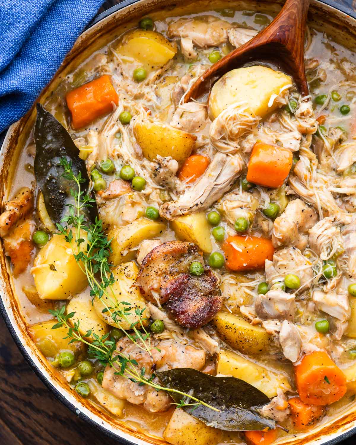 Wooden spoon scooping out chicken potato pea stew.