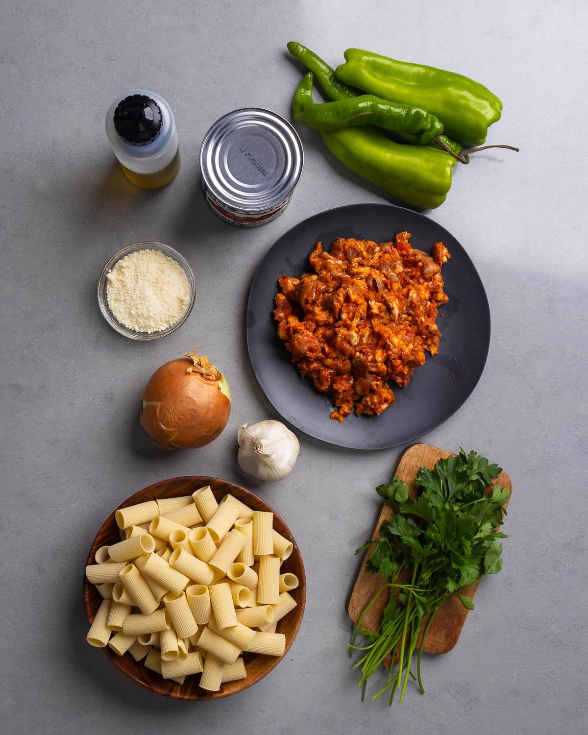 Ingredients shown: olive oil, canned tomatoes, cubanelle peppers, parmesan cheese, fresh chorizo, onion, garlic, rigatoni, and parsley.