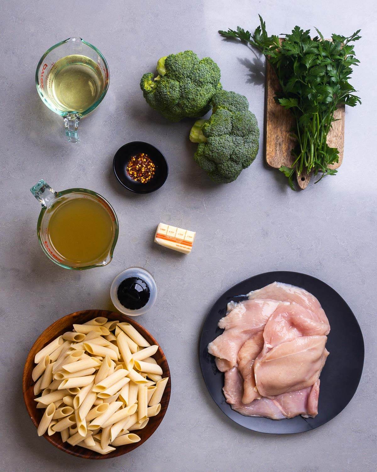 Ingredients shown: wine, broccoli, parsley, hot red pepper flakes, chicken stock, butter, olive oil, penne pasta, and chicken breasts.