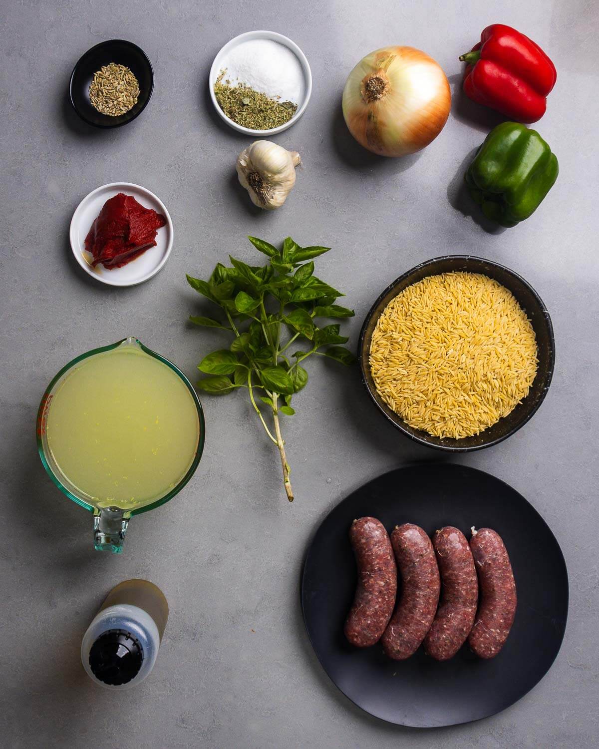 Ingredients shown: fennel seeds, oregano, salt, onion, bell peppers, tomato paste, garlic, basil, chicken stock, orzo, olive oil, and Italian sausage.