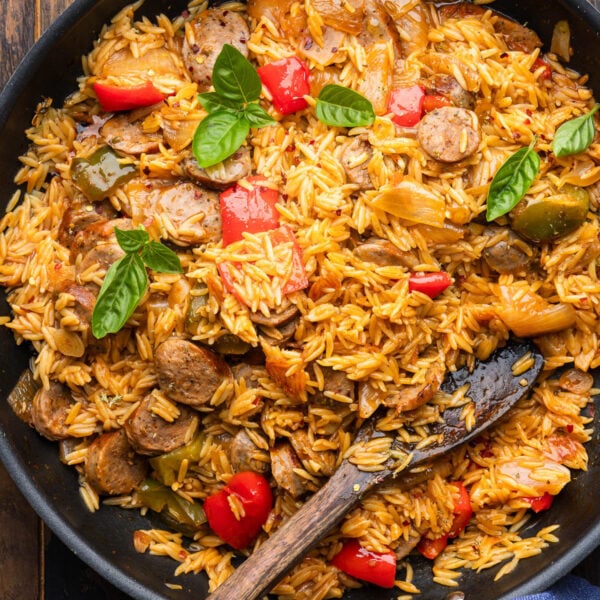 Large pan with sausage peppers orzo garnished with basil leaves.