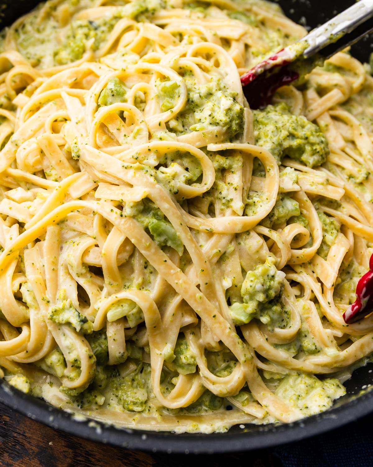 Tongs grabbing broccoli alfredo.