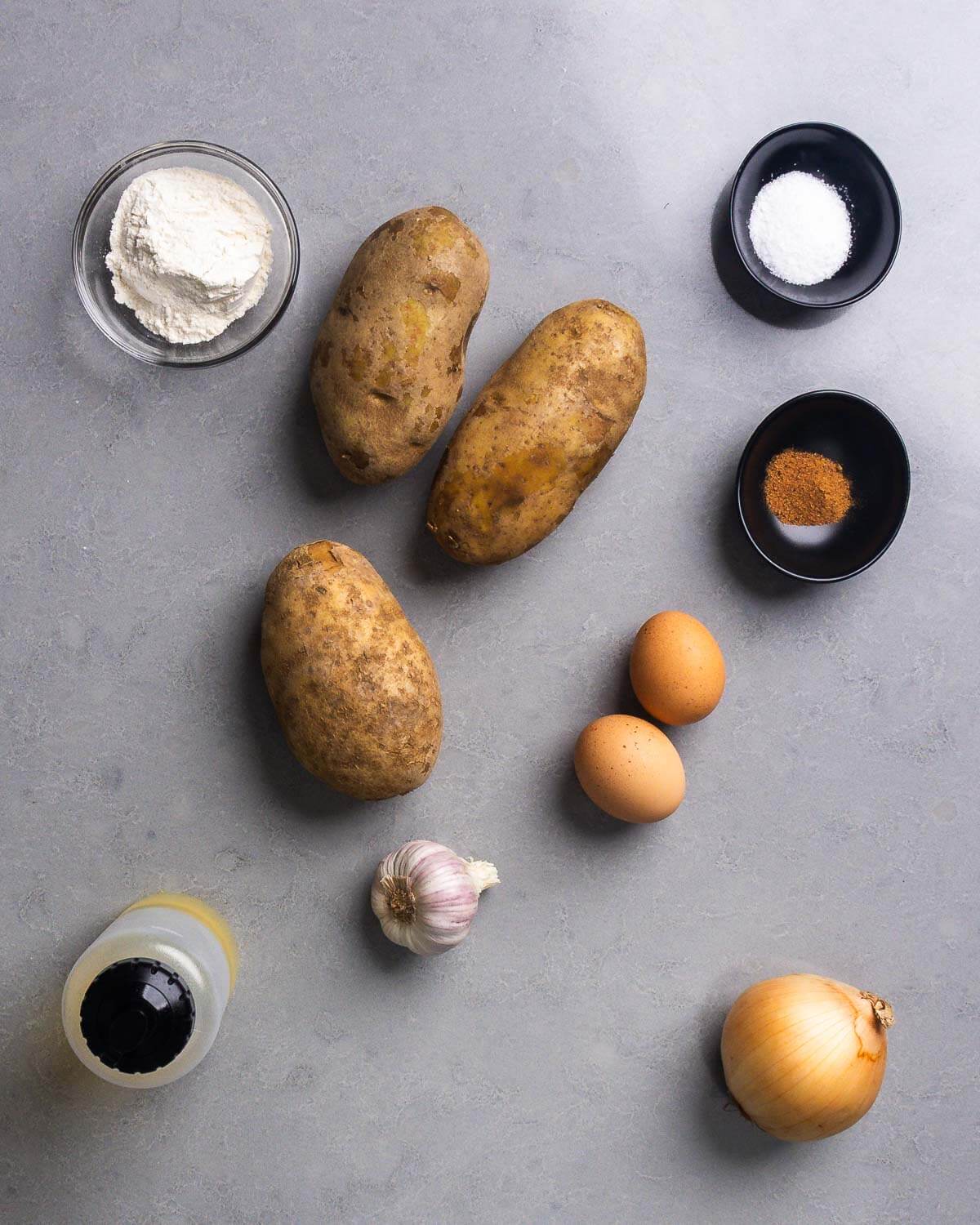 Ingredients shown: flour, potatoes, salt, nutmeg, eggs, garlic, neutral oil, and an onion.