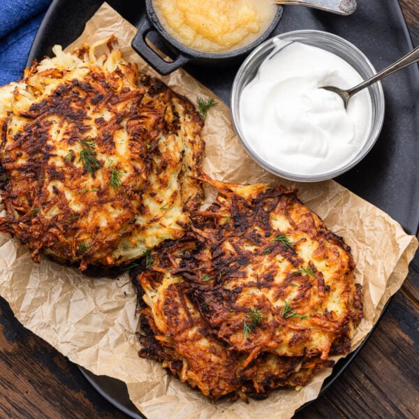 Black platter with German potato pancakes with applesauce and sour cream on the side.