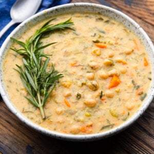 Large white bowl of Greek-inspired chickpea soup garnished with rosemary.