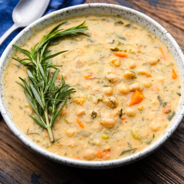 Large white bowl of Greek-inspired chickpea soup garnished with rosemary.