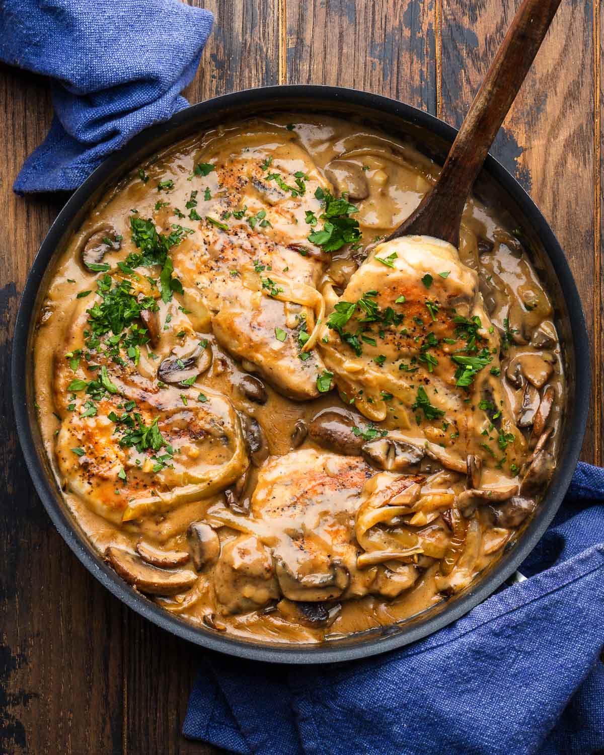 Smothered pork chops in large black pan.