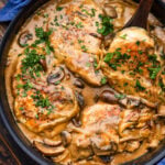 Smothered pork chops topped with parsley in large black pan.