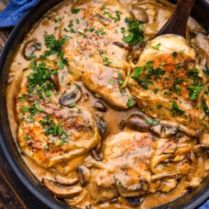 Smothered pork chops topped with parsley in large black pan.