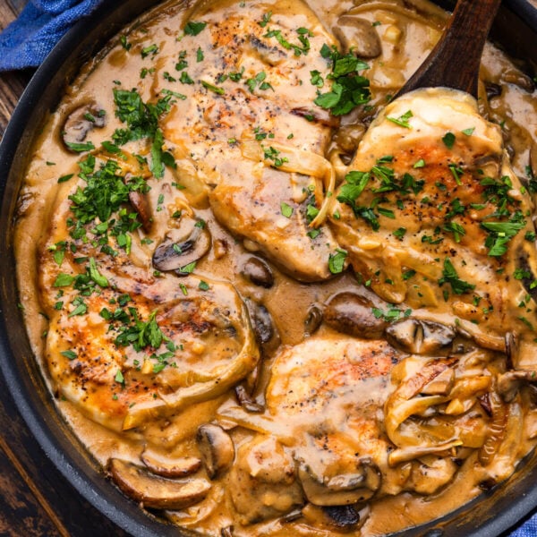 Smothered pork chops topped with parsley in large black pan.