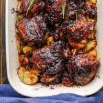 Baking dish with balsamic chicken and potatoes topped with rosemary garnish.