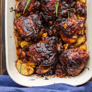 Baking dish with balsamic chicken and potatoes topped with rosemary garnish.