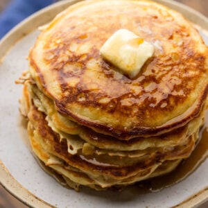 Stack of buttermilk pancakes on plate topped with butter and syrup.