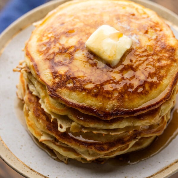 Stack of buttermilk pancakes on plate topped with butter and syrup.