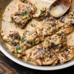 Large stainless pan with chicken au poivre and spoon scooping the sauce.