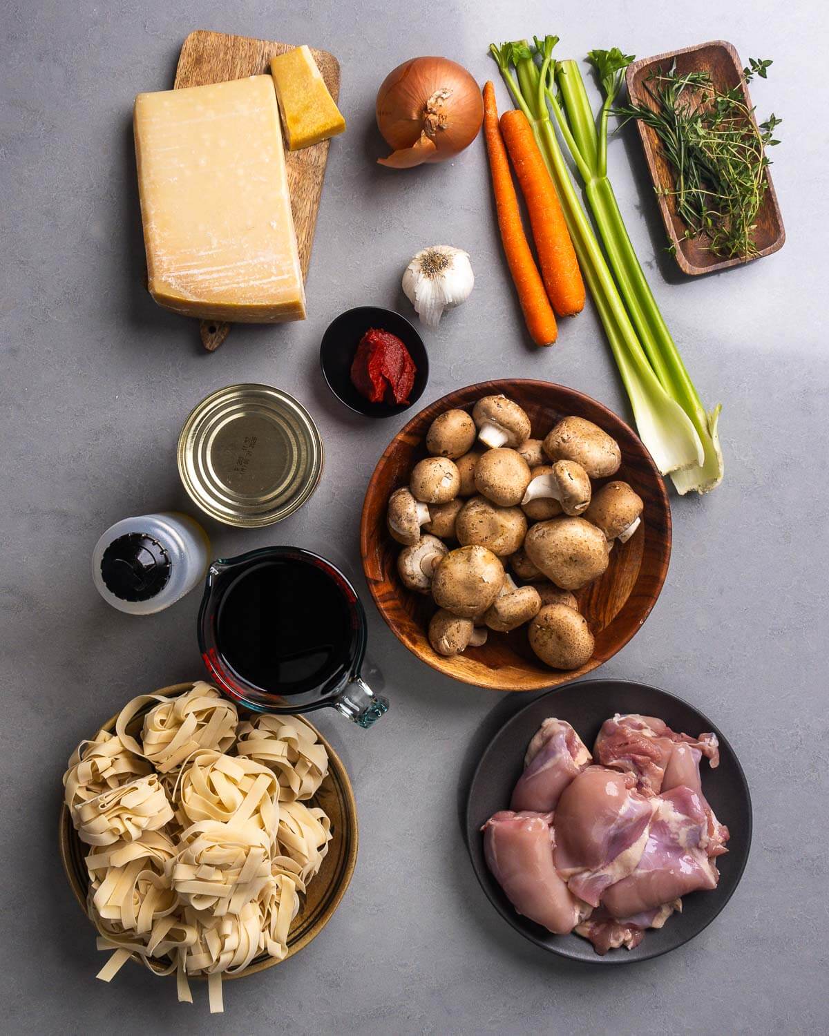 Ingredients shown: parmigiano reggiano block and rind, onion, garlic, tomato paste, carrots, celery, thyme, rosemary, canned tomatoes, olive oil, red wine, mushrooms, pappardelle, and boneless skinless chicken thighs.