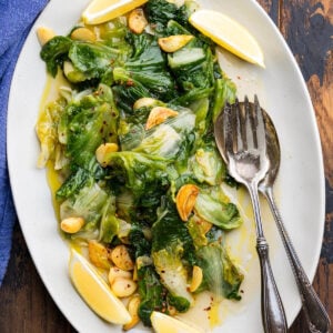 Platter of escarole with garlic and oil served with lemon wedges.