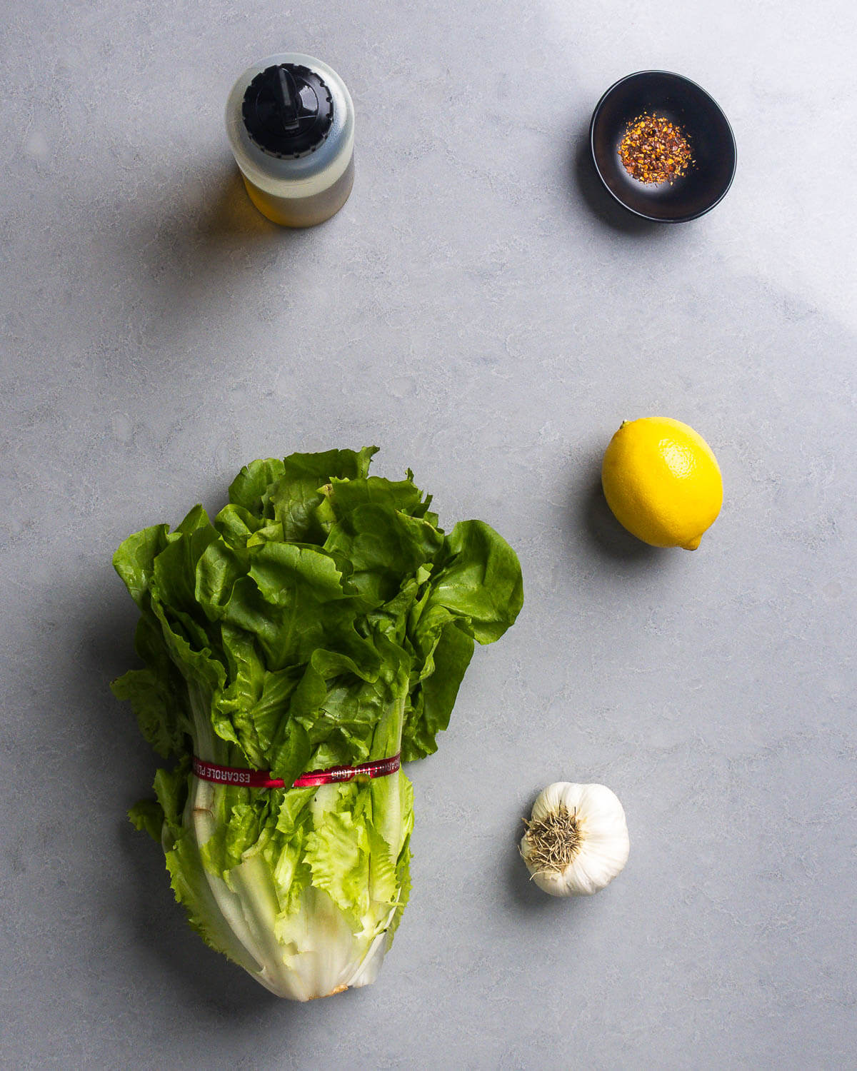 Ingredients shown: olive oil, hot red pepper flakes, head of escarole, lemon, and garlic.