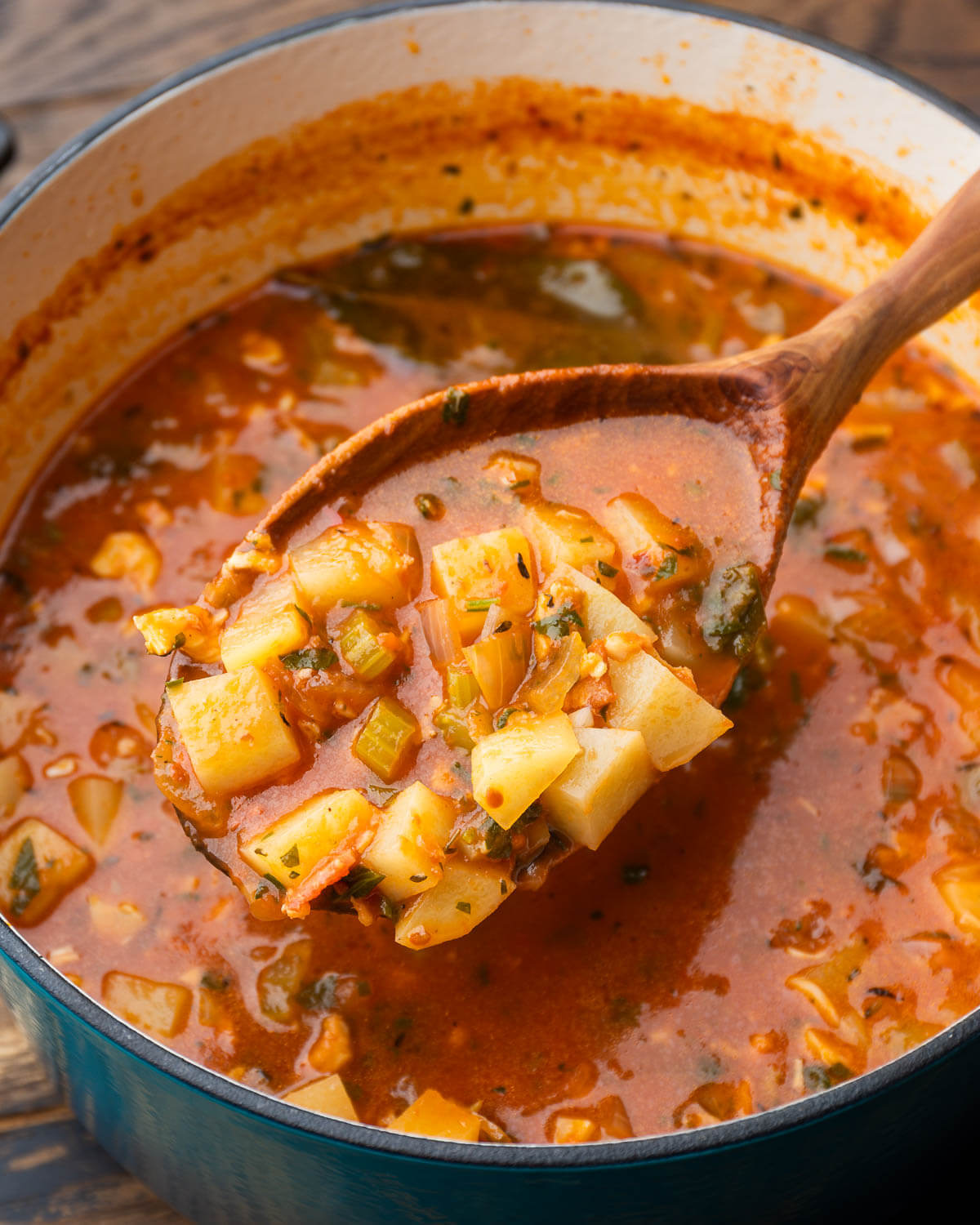 Large wooden spoon holding ladle of Manhattan clam chowder.