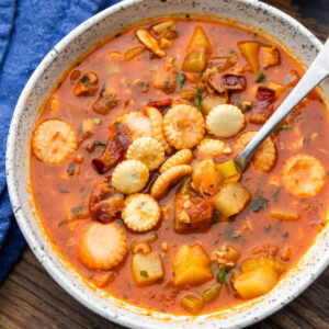 White bowl with Manhattan clam chowder topped with bacon and oyster crackers.